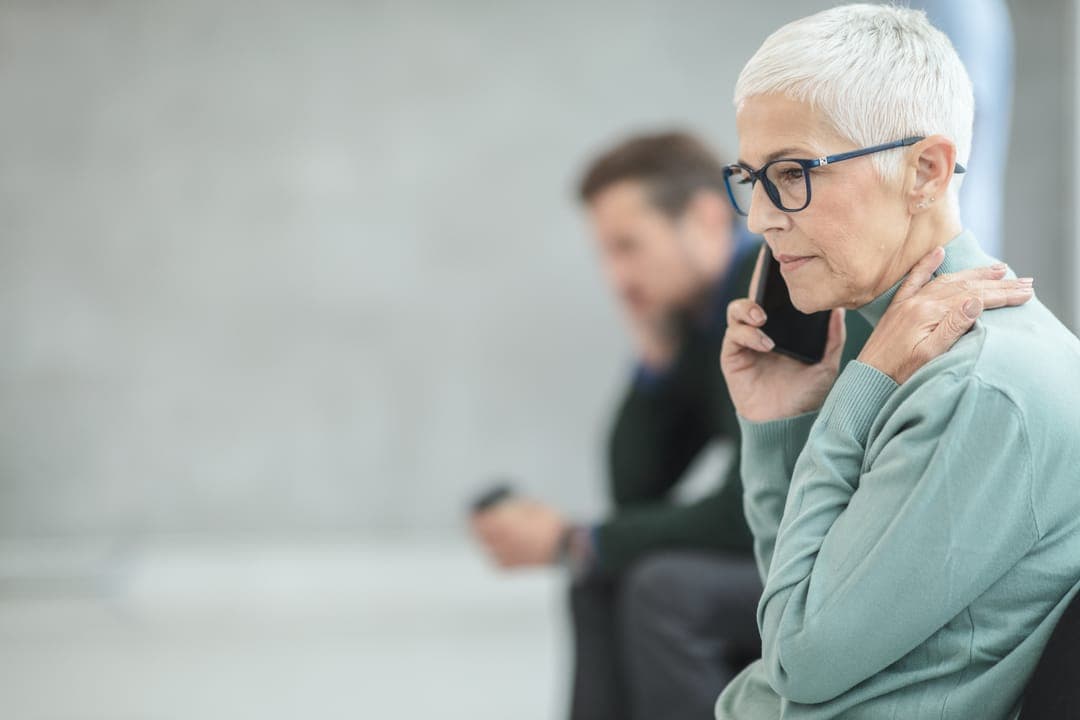 Une femme âgée à lunettes au téléphone, près d'une fenêtre.