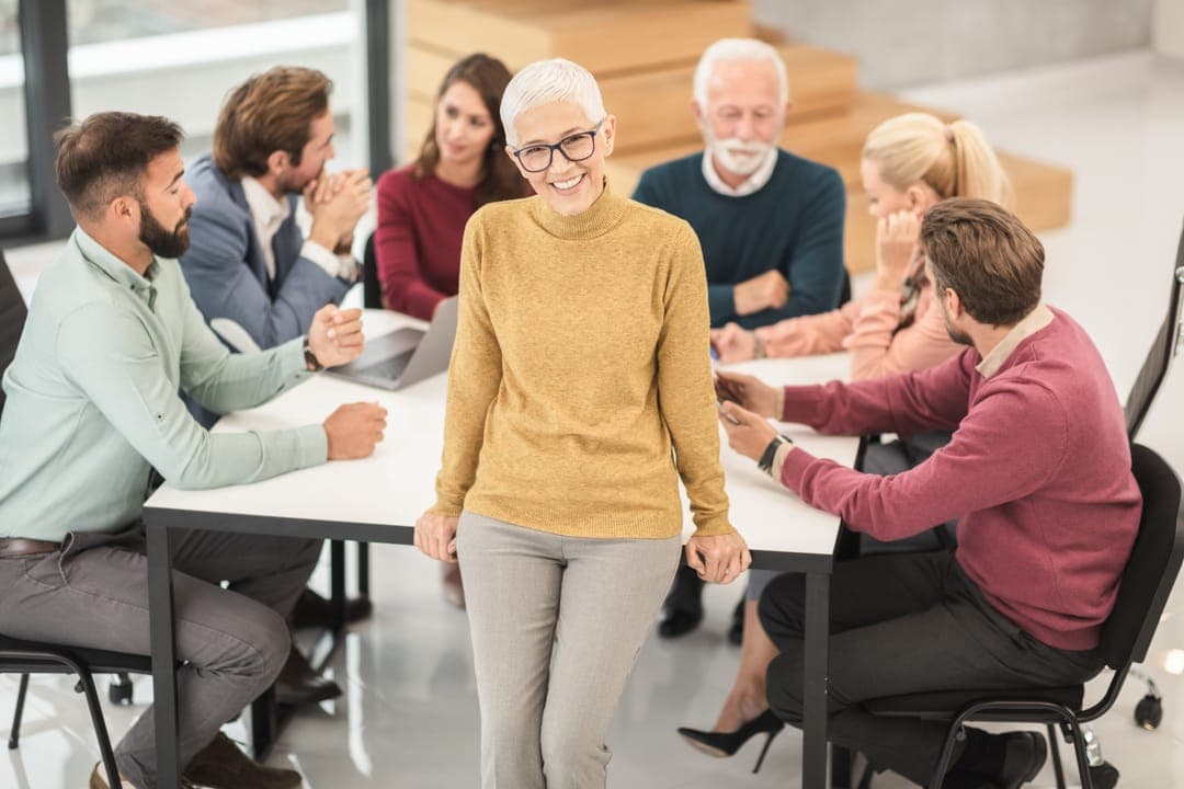 Une équipe réunie autour d'une table, une femme debout au centre, souriante.