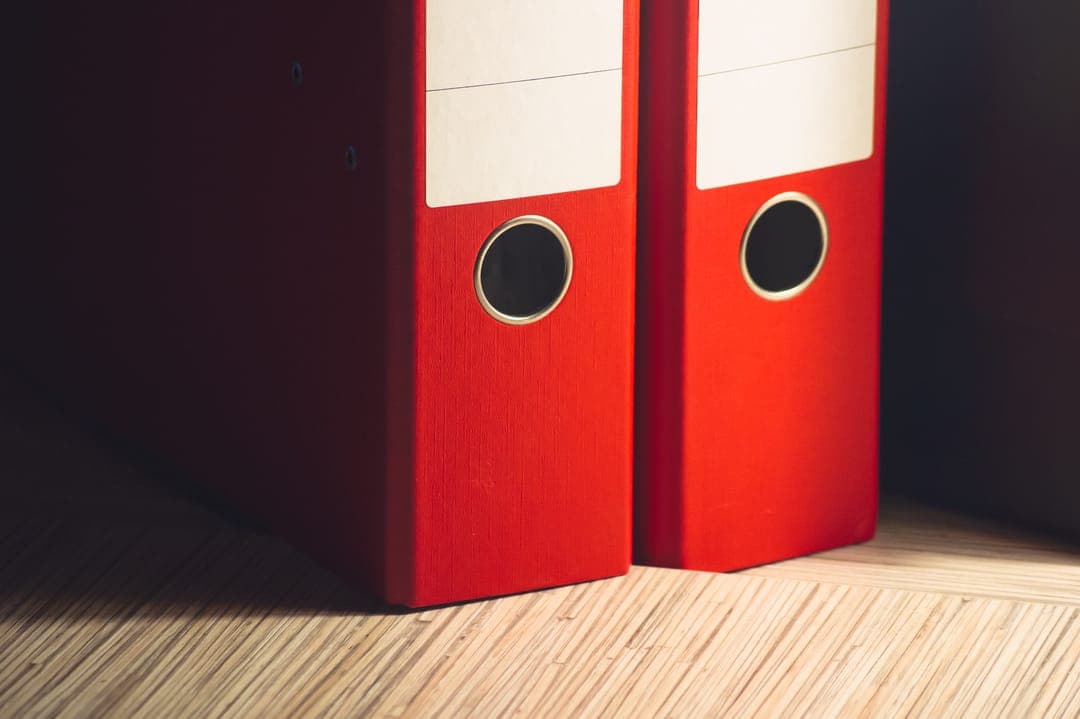 Deux classeurs rouges posés sur un parquet.