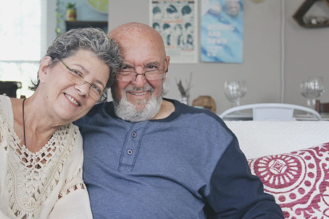 Un couple âgé souriant, chez lui.