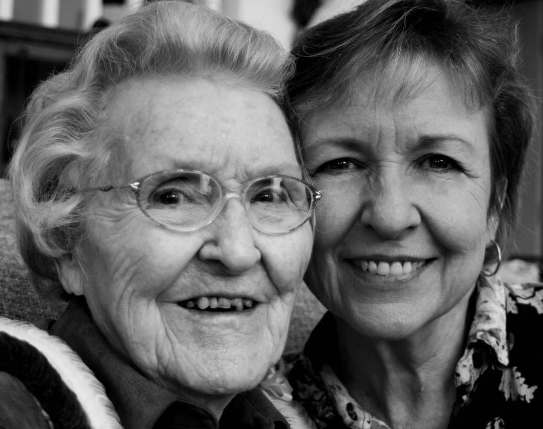 Deux femmes âgées souriantes, en noir et blanc.