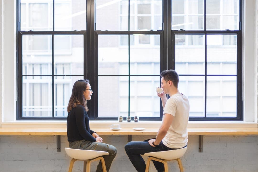 Deux personnes en entretien à une table, devant une grande fenêtre.